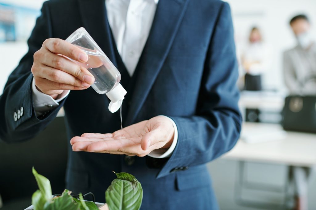 Young businessman in suit dripping sanitizer from plastic bottle on his hands